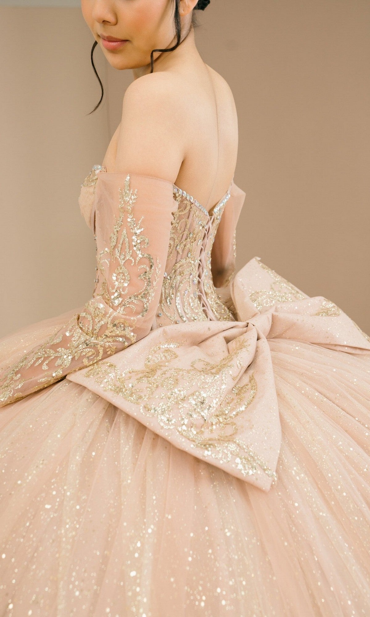 Woman in the Quinceanera Dress 8545JQ By Cinderella Couture, a sparkling ball gown with gold embroidery, large back bow, and off-the-shoulder sweetheart neckline, shown from shoulders down against a neutral background.